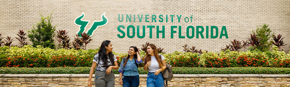 Three students walking by the ֱ sign on campus.