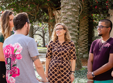 A professor chats with three students outside on campus