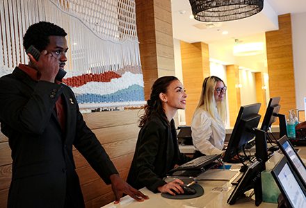 Three hospitality students work behind the desk of a hotel