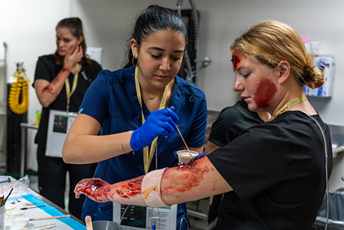 A student applies fake blood, or moulage, to the arm of another student to simulate injuries with astonishing authenticity.