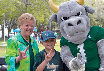 President Law, at left, poses with a little boy in a ֱ number one jersey and Rocky to the right make the ֱ bulls hand signal on a the MLK Plaza on a bright, sunny spring day at the first ֱ Family Fest.