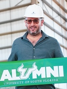 head shot of ֱ alumnus Rene Jacir, a middle-aged Latin male wearing a hard hat and a drak green-blue shirt and holding a ֱ alumni banner